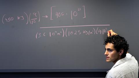A student writes a math equation on a chalkboard.
