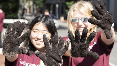 Students hold up their muddy gloves while participating in Global Day of Service
