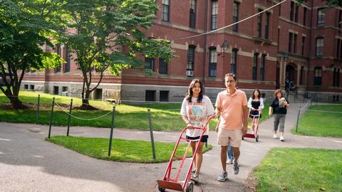 First-year student and their parent walk past a firt-year dorm through the Yard with a dolly during move-in.